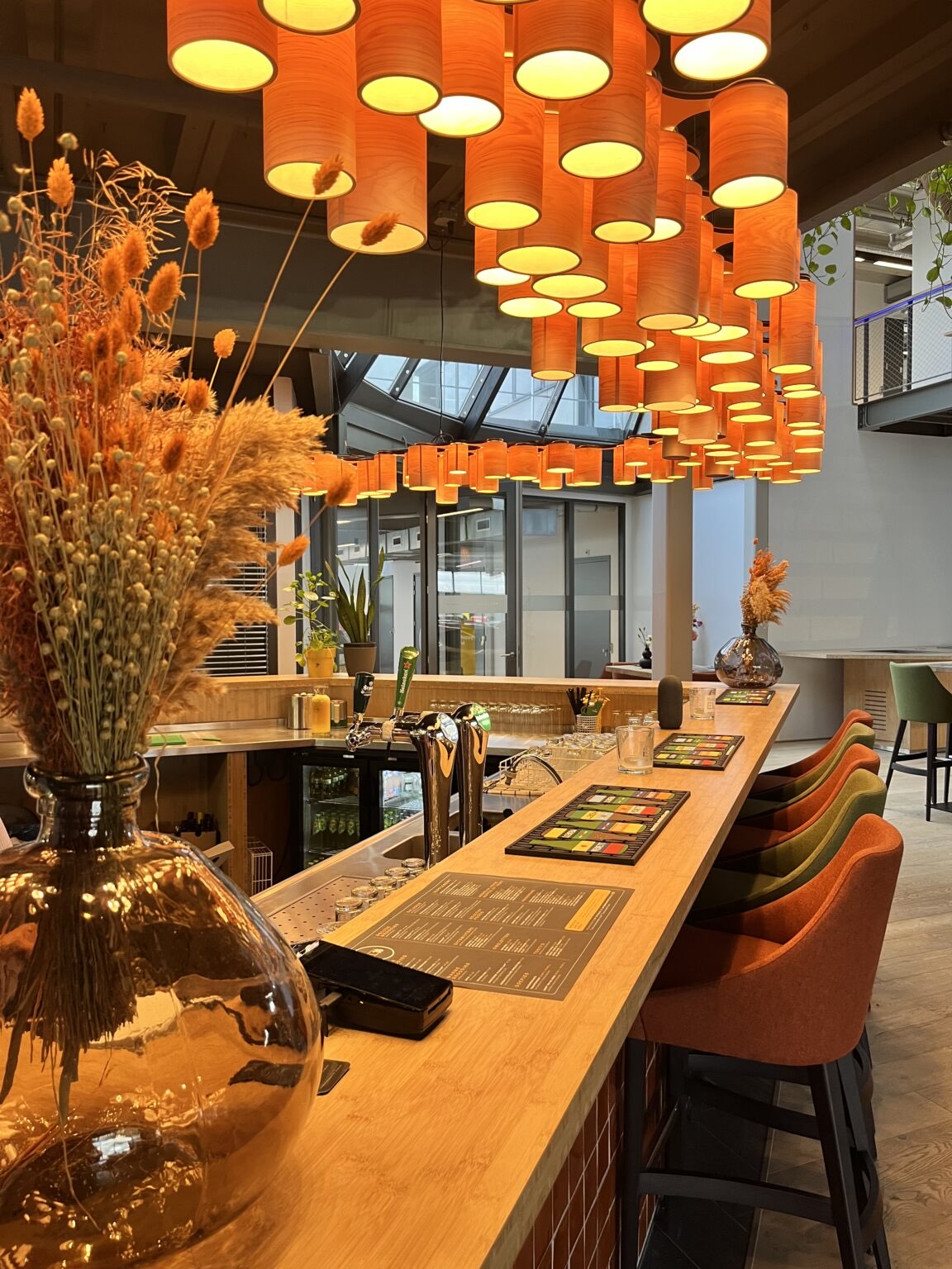 De houten bar van Brasserie EL30 onder een wolk van oranje lampenkappen